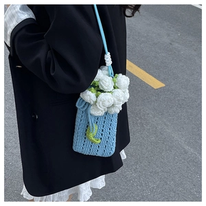 Detail of light blue knit crossbody bag with white 3D flowers on a black blazer