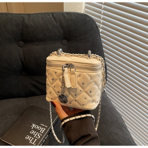 Dettaglio della borsa trapuntata beige con borchie di cristallo e ciondolo rosa