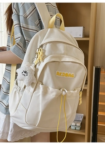Close-up of a cream pleated nylon backpack with a yellow RKDBAG logo and plush star charm