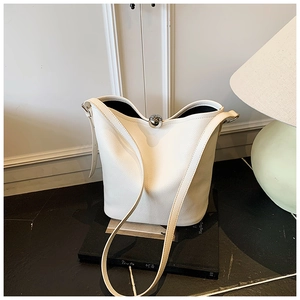 Détail du sac seau en cuir blanc avec fermoir sphérique argenté posé sur des livres