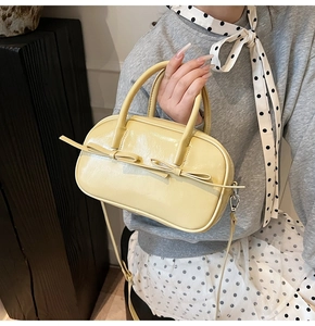 Détail d'un sac à main jaune crème brillant avec doubles nœuds décoratifs et anses rondes