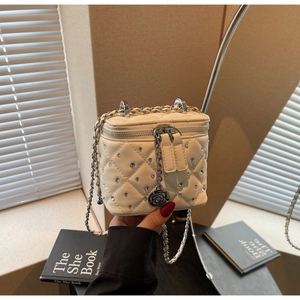 Dettaglio mini borsa trapuntata crema con borchie in cristallo e ciondolo a camelia