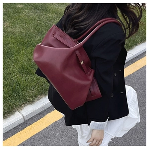 Detail of burgundy leather tote bag side buckle and thin straps on a casual shoulder bag