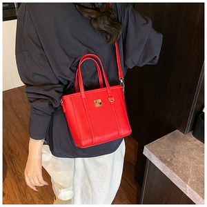Detail of red pebbled leather tote bag with gold metal square accent and shoulder strap