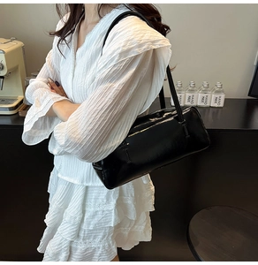 Elegant black glossy shoulder bag styled with a white outfit in a cozy cafe setting