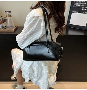 Model wearing high-gloss black patent leather shoulder bag with sleek silver zipper detail