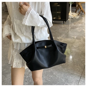 Detail of a black leather tote bag with wing-shaped design and gold metal buckle detail