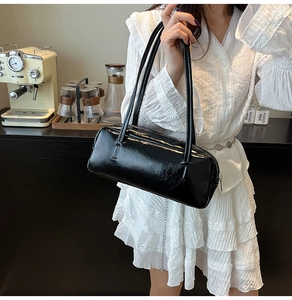 Detailed view of the sleek black glossy rectangular shoulder bag in a stylish cafe setting
