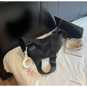 Detail of black nylon crescent bag with wide strap and cute capybara charm on bed
