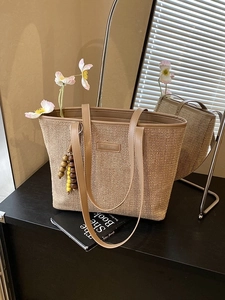Straw beach tote with brown leather trim and colorful bead tassel in a warm indoor setting