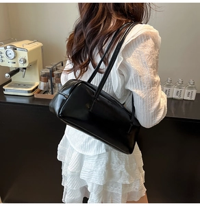 Detailed view of black glossy leather shoulder bag worn by model in a stylish cafe setting