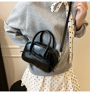 Détail du sac polochon en cuir noir brillant avec décoration de nœud élégant