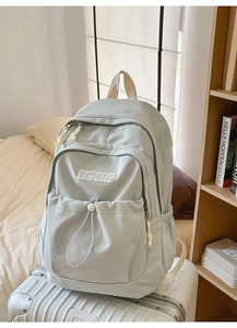 Detail of light blue nylon backpack with white embroidery logo on a white suitcase