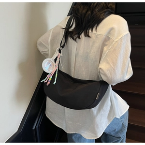 Detail of black crescent crossbody bag with decorative tassel and round white pendant