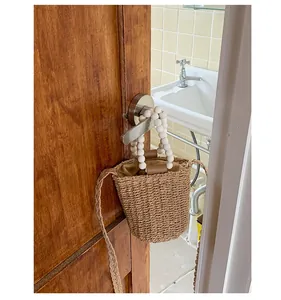 Détail d'un sac seau en paille tissée avec poignée en perles sur porte en bois