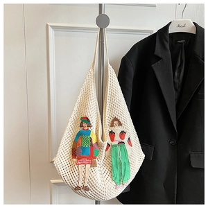 Close-up of cream knit shoulder bag with cartoon embroidery hanging on a hook