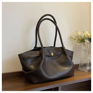 Detail of a dark brown leather tote bag with gold buckle on a minimalist wood shelf