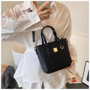 Detail of black lychee grain bucket bag with gold hardware worn as a crossbody bag