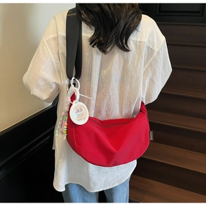 Detail view of a red crescent canvas bag with black strap and cute capybara pendant