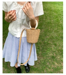Détail d'un sac seau en paille tressée avec anse en perles blanches et bandoulière