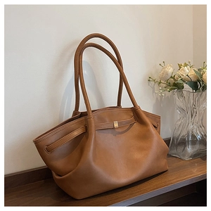 Detail view of a caramel brown leather tote bag on a wooden table with soft lighting