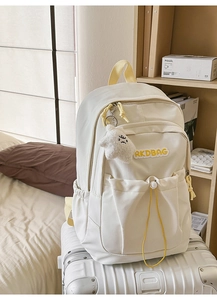 Detail of cream nylon backpack with yellow handles and star plush charm on suitcase