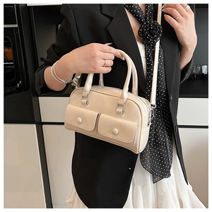 Detail of beige Boston handbag with decorative front pockets and silver hardware on a model