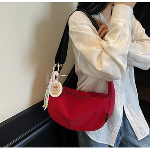 Close-up of red crescent crossbody bag with black strap and capybara charm on model