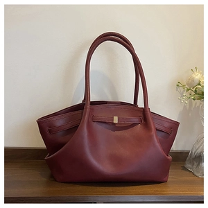 Detail of burgundy tote bag showing soft matte texture and gold buckle on wood table