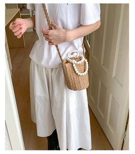 Détail du mini sac seau en paille avec poignée en perles blanches et bandoulière tissée