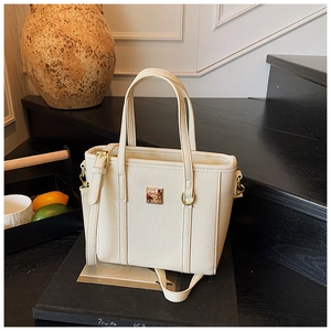 Detail of cream lychee texture leather bucket bag with gold hardware on a dark pedestal