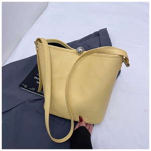 Détail du sac seau en cuir jaune avec fermoir boule argentée sur une veste grise