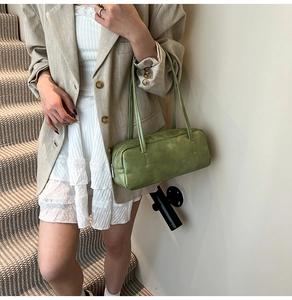 Close-up of a green baguette bag with slim straps worn over the shoulder by a model