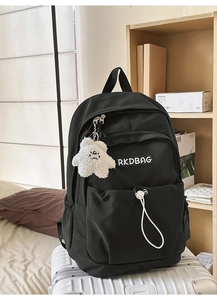 Close-up of black nylon backpack with RKDBAG label and cute monster keychain on a suitcase