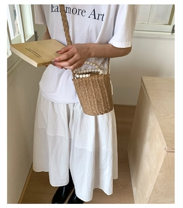 Détail d'un sac seau en paille avec poignée en perles et bandoulière tressée