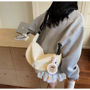Detail of a beige canvas dumpling bag featuring a cute capybara charm and wide strap