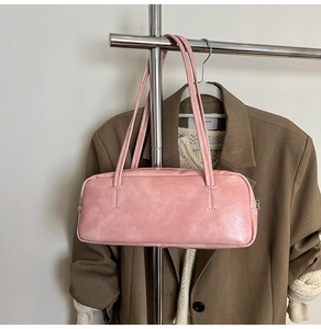 Detailed view of pink leather barrel bag hanging against a warm aesthetic background