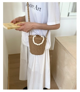 Détail du sac seau en rotin tressé avec poignée en perles blanches et bandoulière assortie