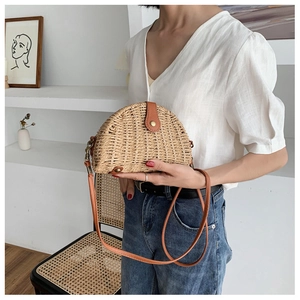 Detail of a semi-circular straw crossbody bag with brown leather flap on a model