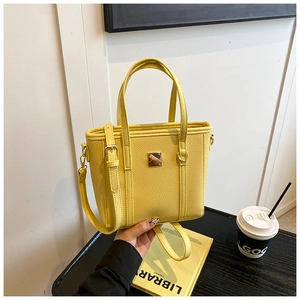 Detail of yellow lychee pattern PU leather handbag with gold metal clasp on a black table