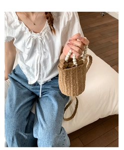 Détail du sac seau en rotin tressé avec poignée en perles blanches et cordon de serrage
