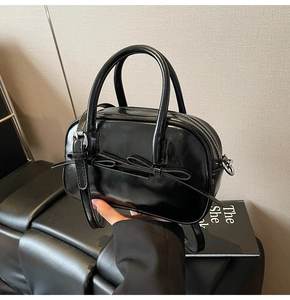 Détail d'un sac polochon en cuir PU brillant noir avec nœud décoratif et zip argenté chic
