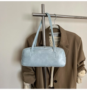 Detail of light blue rectangular shoulder bag featuring dual long straps on a hanger