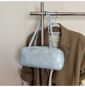 Detail view of a light blue leather shoulder bag with vertical stitching on a hanger