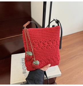 Detail of red hollow-woven tote bag with strawberry charms and black leather straps