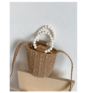 Détail du sac seau en paille avec poignées en perles de bois blanc et doublure