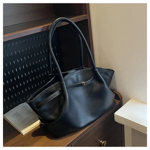 Detail of black leather tote bag featuring gold buckle and elegant wavy rim on wooden desk