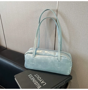 Detail of light blue glossy faux leather pillow bag with long shoulder straps and top zipper