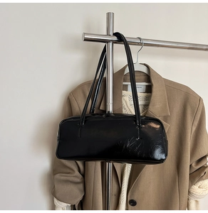 Close-up of a black glossy leather underarm bag featuring minimalist rectangular silhouette