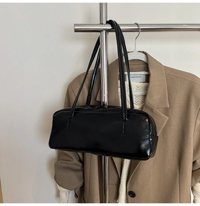 Detail of high-gloss black patent leather baguette bag hanging on a metal hanger